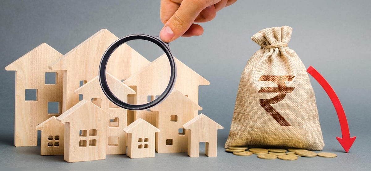 Magnifying glass over wooden houses and a money bag with a Rupee symbol and a downward arrow