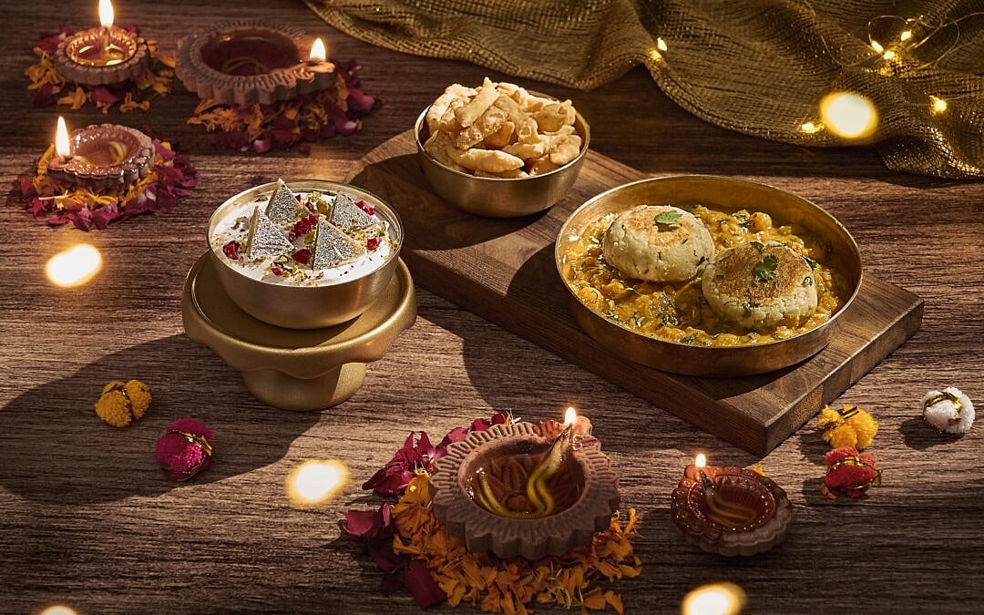An arrangement of Indian sweets and savory snacks with lit diyas and flower petals.