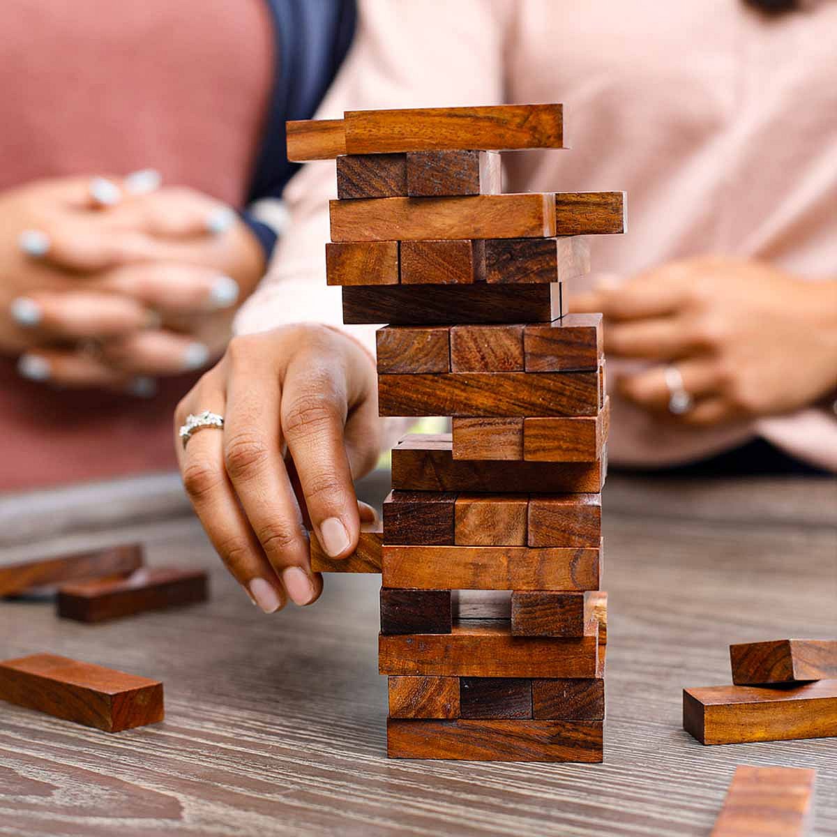 Close-up of a person carefully pulling a block from a tall Jenga tower.