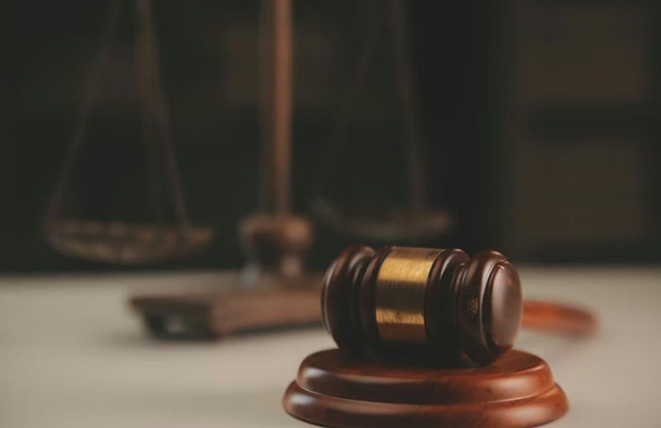 A gavel on a wooden base with scales of justice blurred in the background, illustrating law.