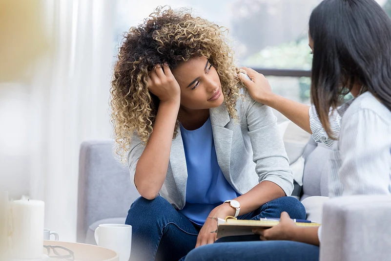 A woman sitting with another woman with her hand placed on her head