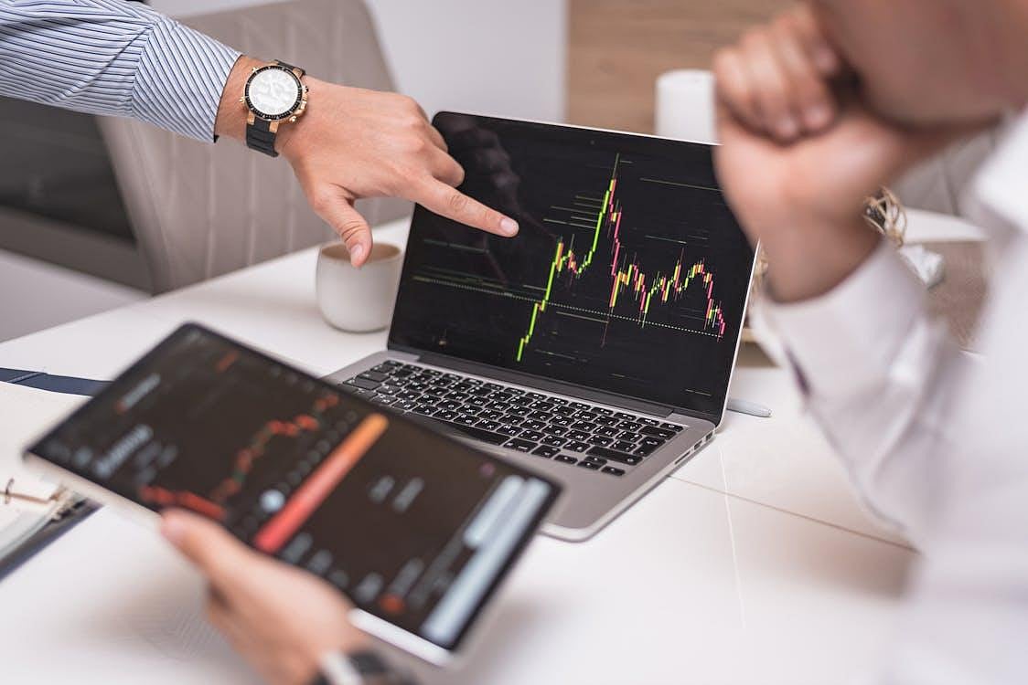 Two people analyzing financial charts on a laptop and tablet during a stock market discussion