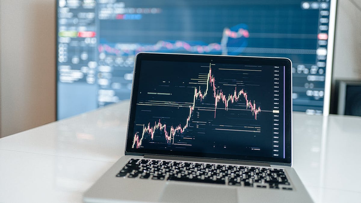 Laptop displaying a financial trading chart with a larger, blurred screen in the background.