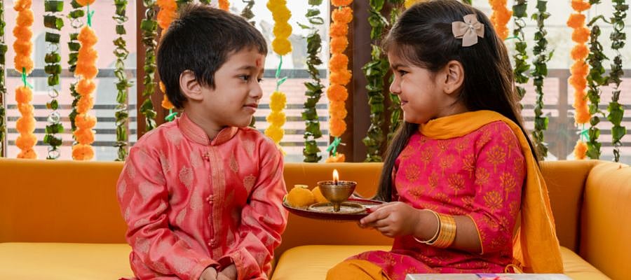 Two children in traditional Indian clothes looking at each other, holding a puja thali.