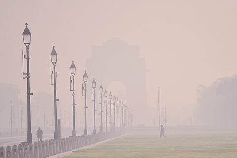 People walk amid low visibility caused by worsening air quality, with India Gate shrouded in haze in the backdrop, in New Delhi.