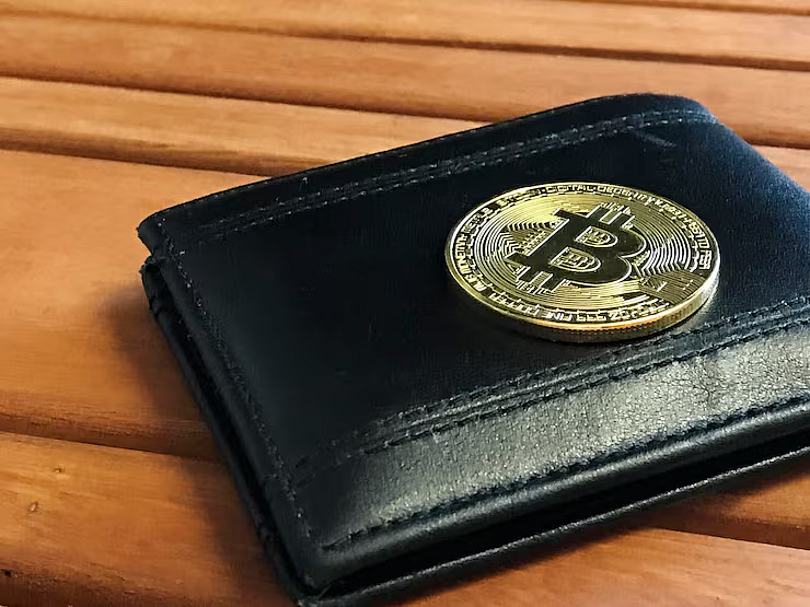 Black wallet with gold bitcoin on wood surface