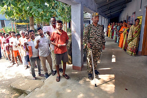 A security official keeps vigil as voters wait in queues to cast votes at a polling station during the first phase of the Bihar Assembly elections, in Patna.