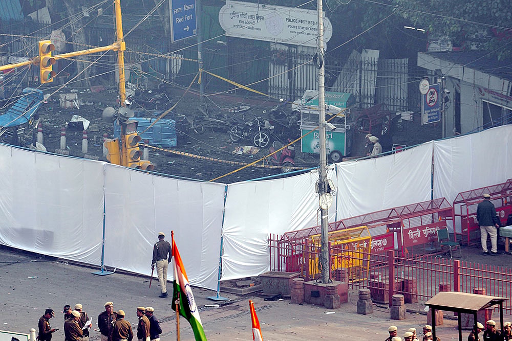 | Photo: PTI/Kamal Kishore : Police personnel near an area covered with white cloth in view of the blast that occurred near Red Fort Metro Station on Monday, killing at least nine people and gutting several vehicles, in New Delhi.