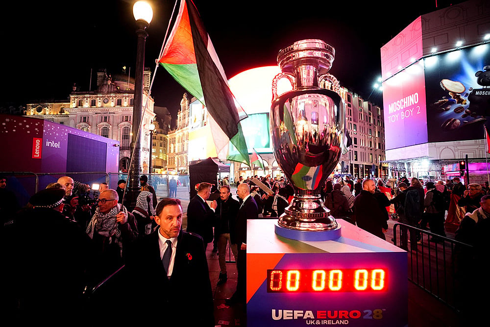 | Photo: James Manning/Pool via AP : A protester speaking with a police officer near a replica UEFA trophy during the Euro 2028 launch at Below The Lights, Piccadilly Circus, London.