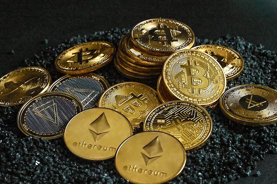 A pile of various physical cryptocurrency coins, including Bitcoin and Ethereum.