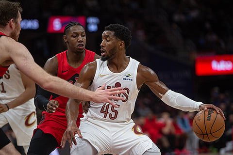 Cleveland Cavaliers' Donovan Mitchell (45) keeps the ball from Toronto Raptors' RJ Barrett, rear, and Jakob Poeltl, left, during the second half of an NBA basketball game in Cleveland.