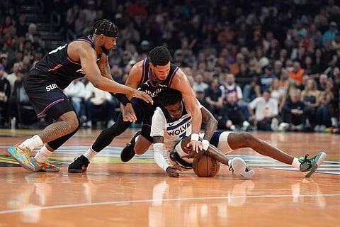 Phoenix Suns guards Jordan Goodwin, left, and Devin Booker, top right, fight for the ball with Minnesota Timberwolves forward Jaden McDaniels, bottom right, during the first half of an NBA basketball game in Phoenix. 