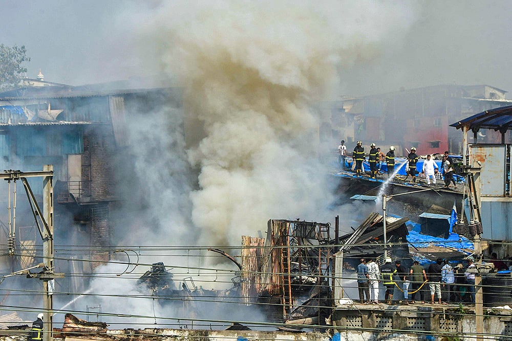 | Photo: PTI : Smoke billows as firemen douse a fire breaking out in huts close to the Harbour line local train tracks at Dharavi area, in Mumbai, Maharashtra.