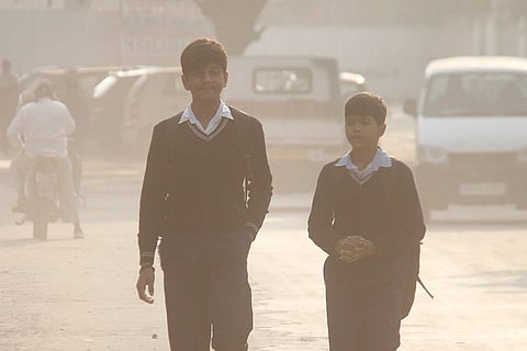 Students walk along a road amid low visibility as air quality deteriorates, in Gurugram.