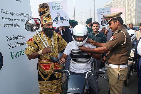 A police official distributes a helmet to a commuter riding without helmet as part of an awareness campaign, in Noida, Gautam Buddha Nagar district.