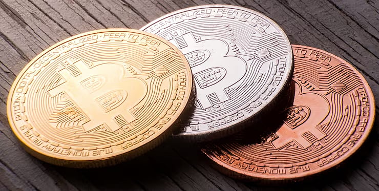 Three cryptocurrency coins (Bitcoin) on a dark surface.