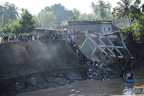 
People walk down the embankment of a river to take a boat ride across after a bridge nearby collapsed during a flood in Bireun, Aceh province, Indonesia.
