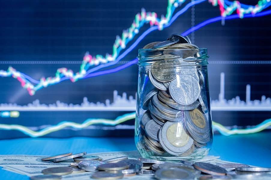 A glass jar full of coins in front of a blue background with a cryptocurrency trading chart