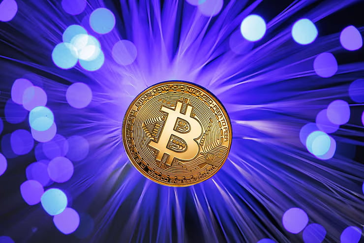 Gold Bitcoin coin glowing at the center of a blue light burst with bokeh effects.