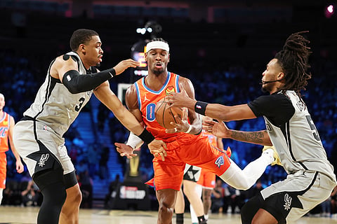 Oklahoma City Thunder guard Shai Gilgeous-Alexander, center, tangles with San Antonio Spurs' Keldon Johnson (3) and Stephon Castle (5) under the net in the first half of an NBA Cup semifinals basketball game in Las Vegas. 