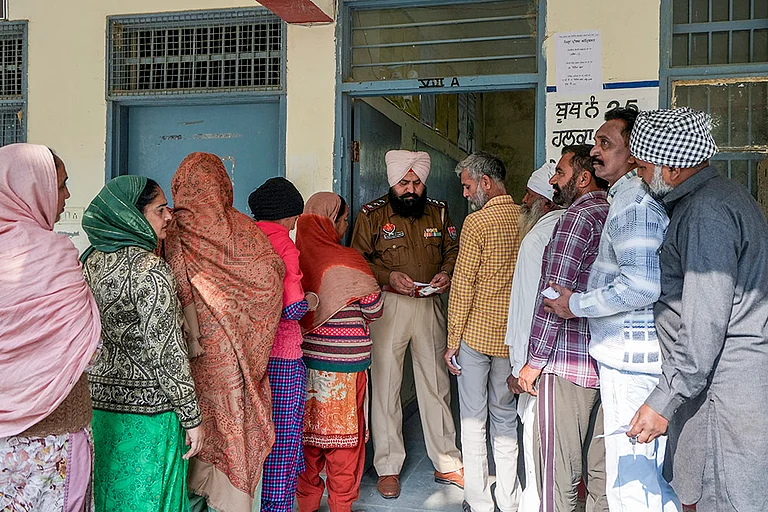 A police official checks documents of voters at a polling station during 'Zila Parishad' and 'Panchayat Samiti' elections, on the outskirts of Amritsar, Punjab. - | Photo: PTI/Shiva Sharma