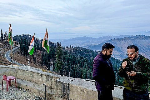 People interact against the backdrop of a valley, in Bhaderwah, Jammu and Kashmir. Tourism sector in J&K’s Bhaderwah faces setback due to the absence of snowfall. 