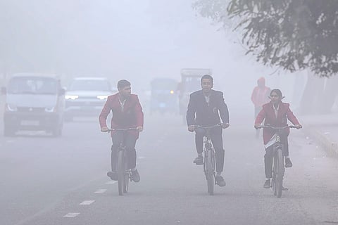 Students ride bicycles along a road shrouded in dense fog on a cold winter morning, in Noida.