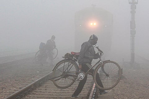 People carry bicycles while crossing a railway track amid low visibility on a cold winter morning, in Gurugram.