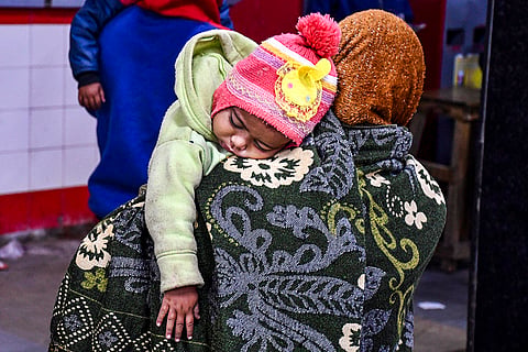 A woman carries a child on a cold winter morning at the railway station, in Prayagraj.