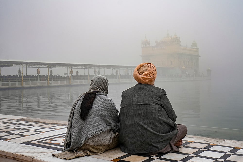 | Photo: PTI/Shiva Sharma : Devotees sit near the 'Amrit Sarovar' at Golden Temple amid dense fog, in Amritsar.
