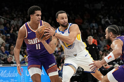 Golden State Warriors guard Stephen Curry, center, looks to pass the ball between Phoenix Suns forwards Oso Ighodaro (11) and Dillon Brooks, right, during the first half of an NBA basketball game in Phoenix. 