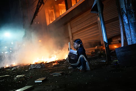 A girl rescues books from a shop near the premises of the Prothom Alo daily newspaper which was set on fire by angry protesters after news reached the country from Singapore of the death of a prominent activist Sharif Osman Hadi, in Dhaka, Bangladesh.