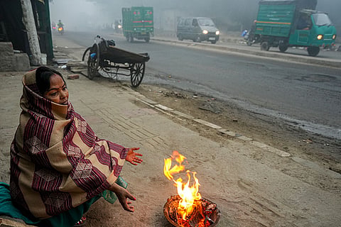 A woman warms herself around a small fire on a foggy winter morning, in New Delhi.
