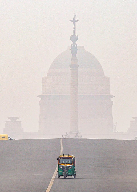An auto passes along Kartavya Path as Rashtrapati Bhavan remains barely visible amid low visibility, in New Delhi.