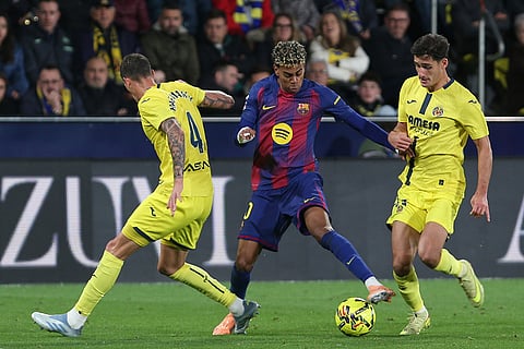 Barcelona's Lamine Yamal, center, vies for the ball with Villarreal's Rafa Marin, left, during the Spanish La Liga soccer match between Villarreal and Barcelona in Villarreal, Spain.