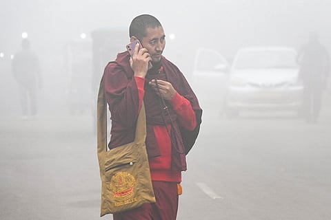 A Buddhist monk talks on a mobile phone while walking near the Mahabodhi Temple complex shrouded in dense fog on a cold winter morning, in Bodh Gaya, Bihar.