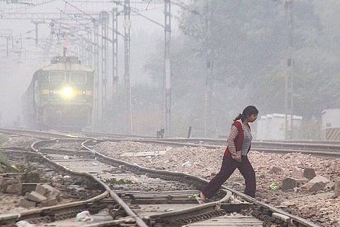 A woman crosses a railway track while a train approaches amid low visibility on a winter morning, in Gurugram.