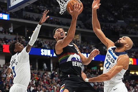 Denver Nuggets forward Spencer Jones, center, drives to the basket between Minnesota Timberwolves forward Jaden McDaniels, left, and center Rudy Gobert in the first half of an NBA basketball game, in Denver. 