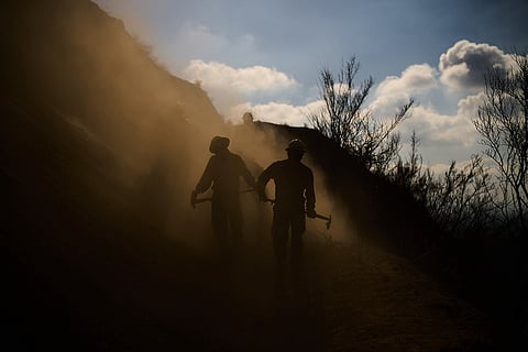Members of the Navajo Scouts firefighter crew kick up dust as they clear debris from a landslide across a road on a hillside as they battle the Eaton Fire, Jan. 17, 2025, in Altadena, California.