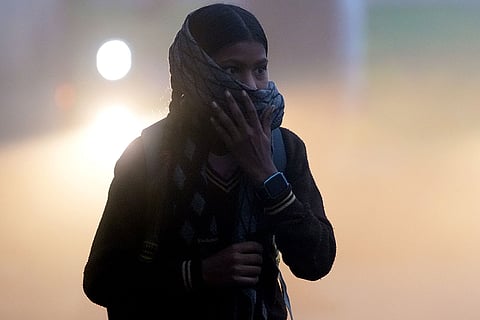 A school girl covers her face as a dense layer of fog engulfs the area, affecting visibility on a winter morning, in New Delhi.