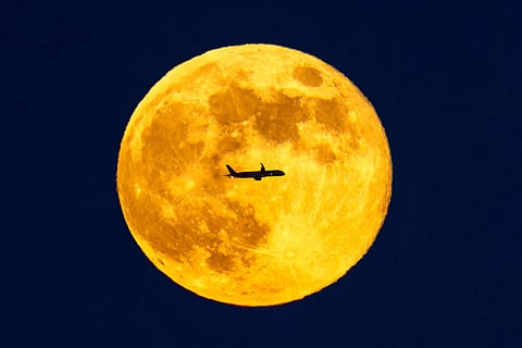 A planes passes across the full moon as it rises over London, seen from Sandown racecourse in Esher, England.