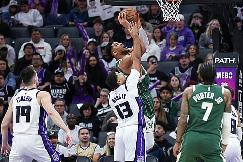 Milwaukee Bucks forward Giannis Antetokounmpo, center background, makes a layup and draws the foul on Sacramento Kings forward Keegan Murray (13) during the second half of an NBA basketball game in Sacramento, California.