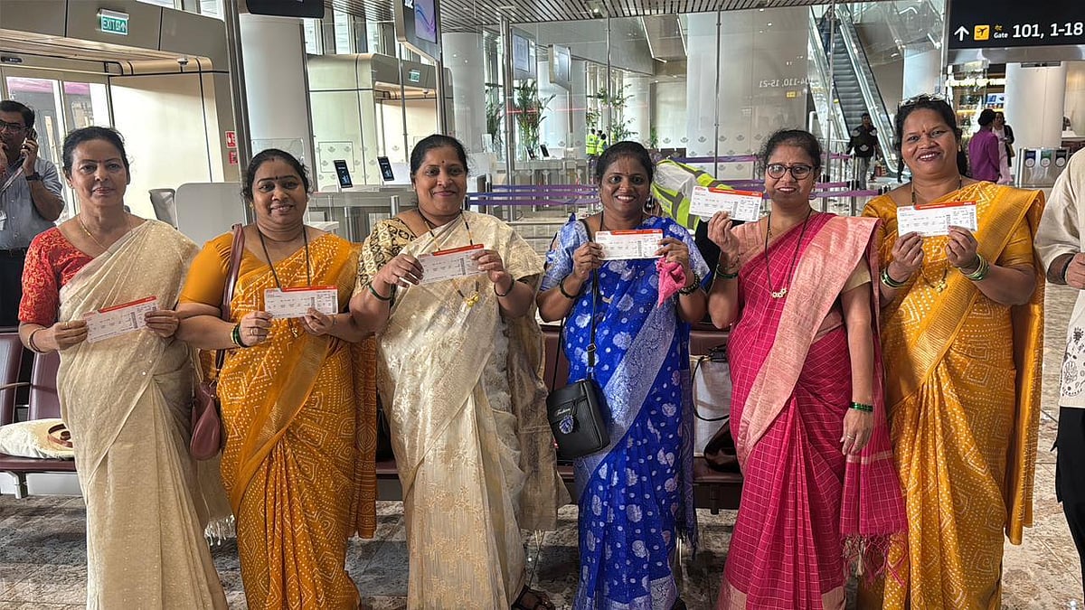 Group of women in colorful sarees stand together in an airport terminal holding boarding passes.