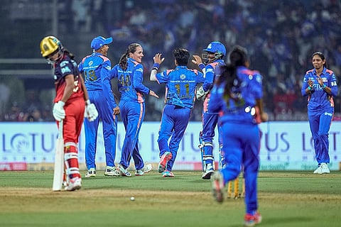 Mumbai Indians’ Amelia Kerr, back second left, celebrates with teammates after taking the wicket of Royal Challengers Bengaluru’s Radha Yadav during a Women's Premier League (WPL) T20 cricket match between Mumbai Indians and Royal Challengers Bengaluru, at the DY Patil Stadium, in Navi Mumbai.