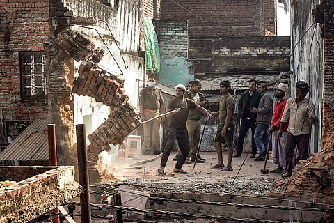 Police personnel look on as workers dismantle structures during the ongoing demolition drive in Dal Mandi area, in Varanasi.