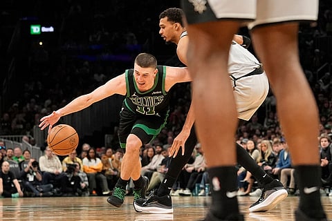 Boston Celtics guard Payton Pritchard goes low to drive by San Antonio Spurs forward Victor Wembanyama during the first half of an NBA basketball game in Boston.