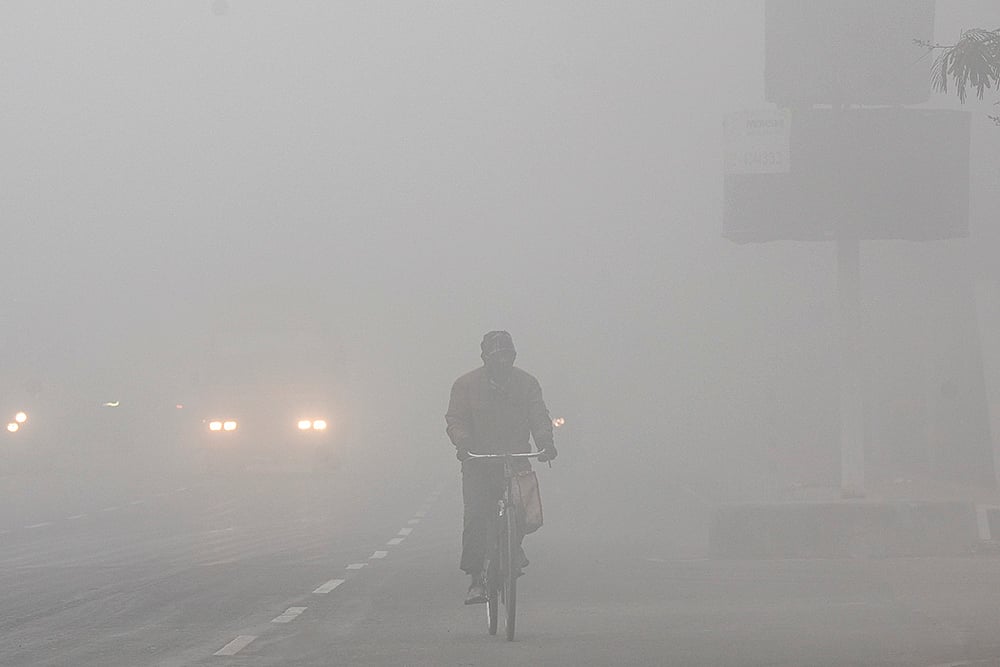 A person cycles through dense fog on a winter morning, in Delhi.