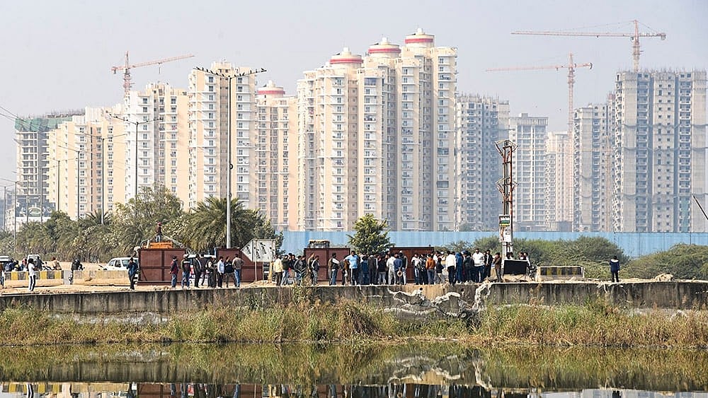 | Photo: PTI : People gather near a water-filled pit at a construction site following the death of a 27-year-old engineer who drowned, in Noida.