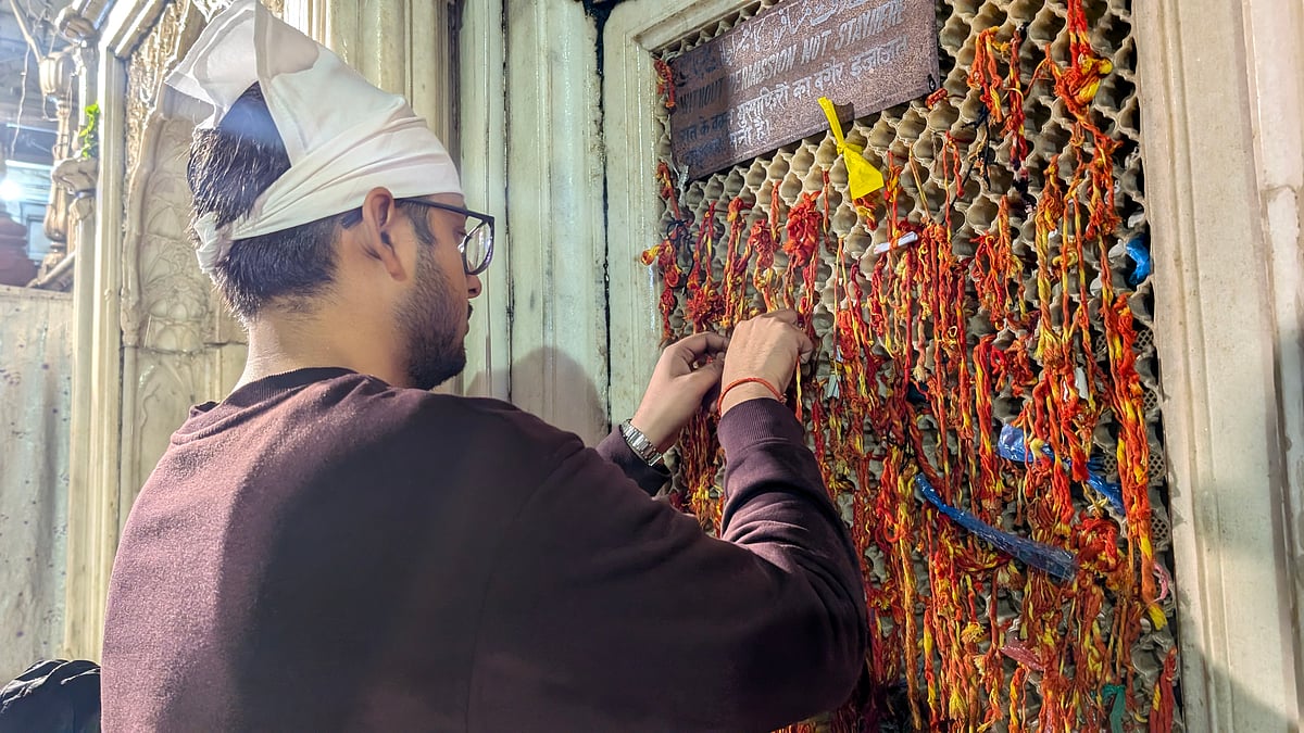 A man ties a sacred thread to the dargahs jaali, knotting hopes and blessings in the downpour.

