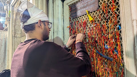 A man ties a sacred thread to the dargah's jaali, knotting hopes and blessings in the downpour.
